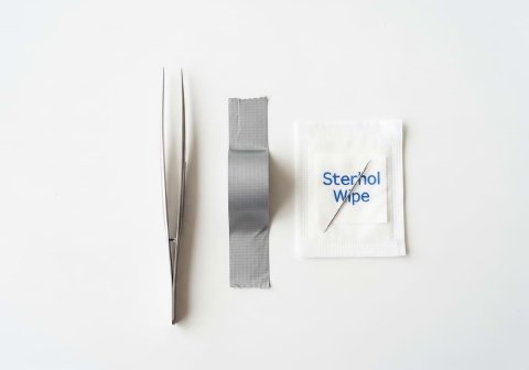 A flat lay of tools for removing cactus needles, including tweezers, tape, and an antiseptic wipe.